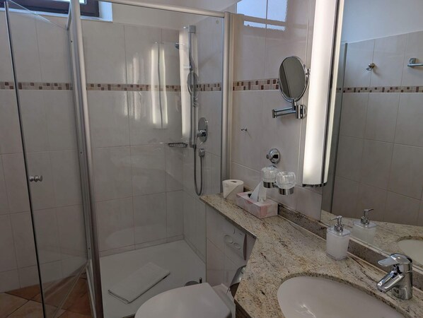 A modern bathroom with a glass-enclosed shower, a vanity with a sink, and a mirror. - Stadthotel Augsburg (Augsburg)