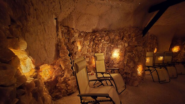 Una habitación con paredes de piedra, varias sillas y mesas, iluminada con luz cálida.