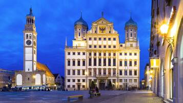 A historic building with a clock tower and two domes, surrounded by cobblestone streets and benches.