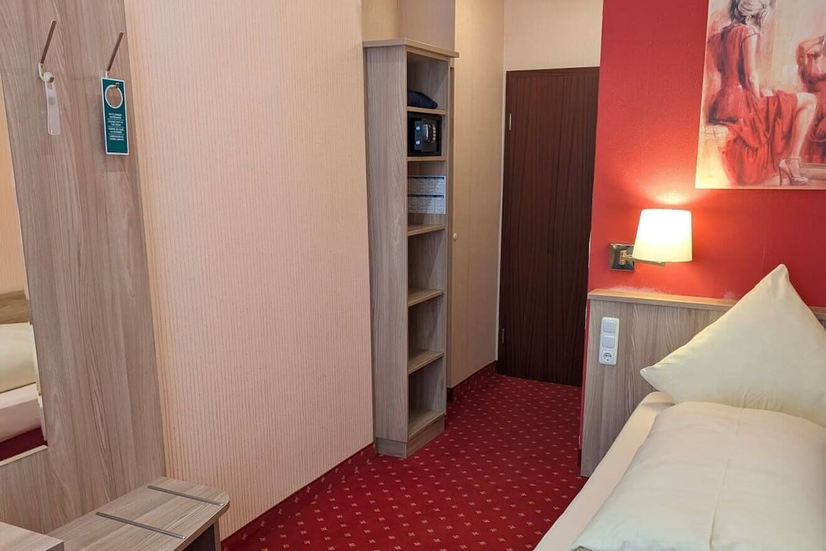 A hotel room with a bed, a desk, a wardrobe, and a shelf unit.