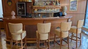 Un área de bar con suelo de mármol, mostrador de madera y varios taburetes de mimbre.