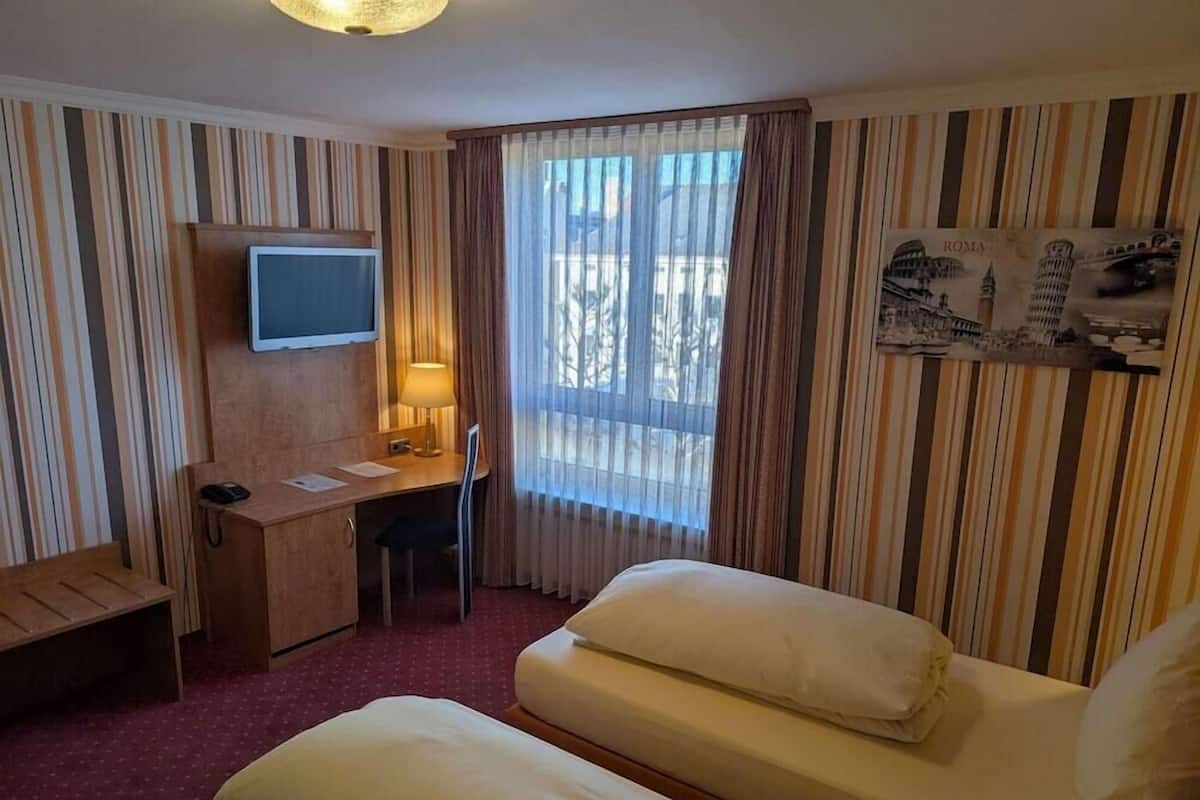 A hotel room with a desk, a television, a bed, and a window with curtains.