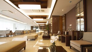 A modern hotel lobby with a spacious layout, a reception desk, comfortable seating areas, and a decorative vase with flowers on a central table. - Tara Hotel Yogyakarta (Yogyakarta)