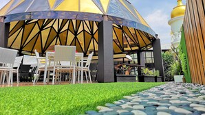 A covered outdoor seating area with chairs and a table, surrounded by a well-maintained lawn and a stone pathway. - Tara Hotel Yogyakarta (Yogyakarta)