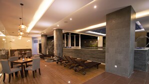 A modern indoor area with a wooden floor, a reception desk, and a seating area with chairs and sun loungers. - Tara Hotel Yogyakarta (Yogyakarta)