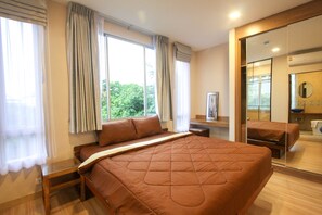 A hotel room with a large bed, a bedside table, a mirror, and a view of greenery outside. - A Good Nite at Nimman (Chiang Mai)