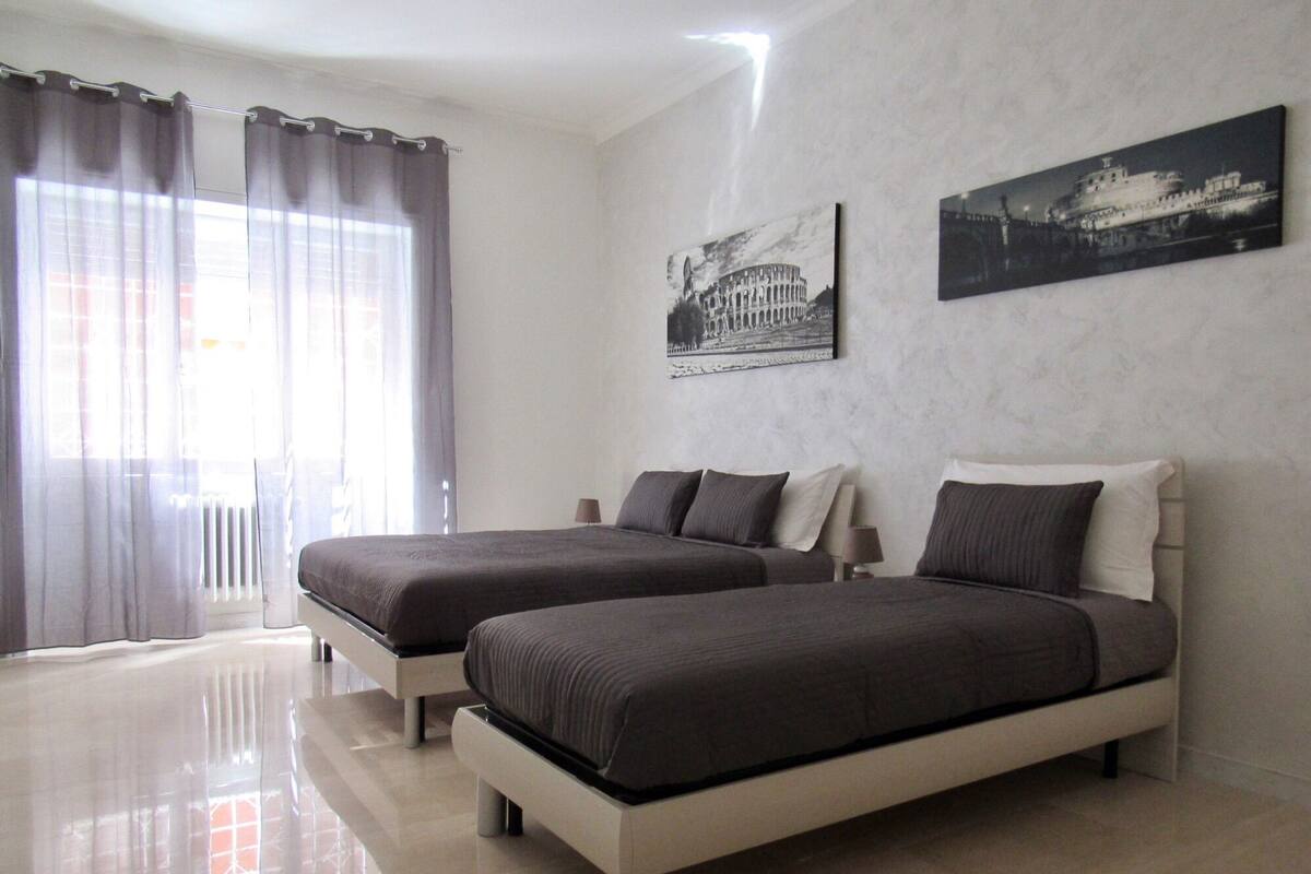 A bedroom with two beds, a window with curtains, and two wall-mounted pictures.