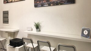 A hotel reception area with two paintings of cityscapes, a guest review plaque, a printer, and a potted plant. - Roema Guest House (Rome)