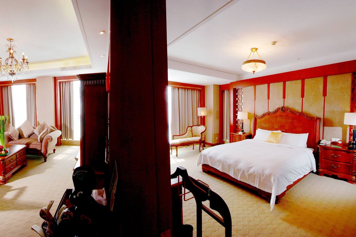 A hotel room with a large bed, a sofa, a chair, a desk, and a chandelier.