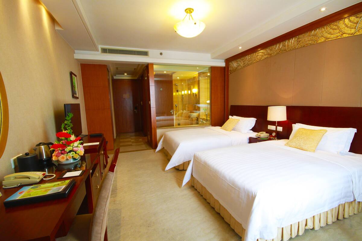 A hotel room with two beds, a desk with a telephone, a lamp, and a mirror.