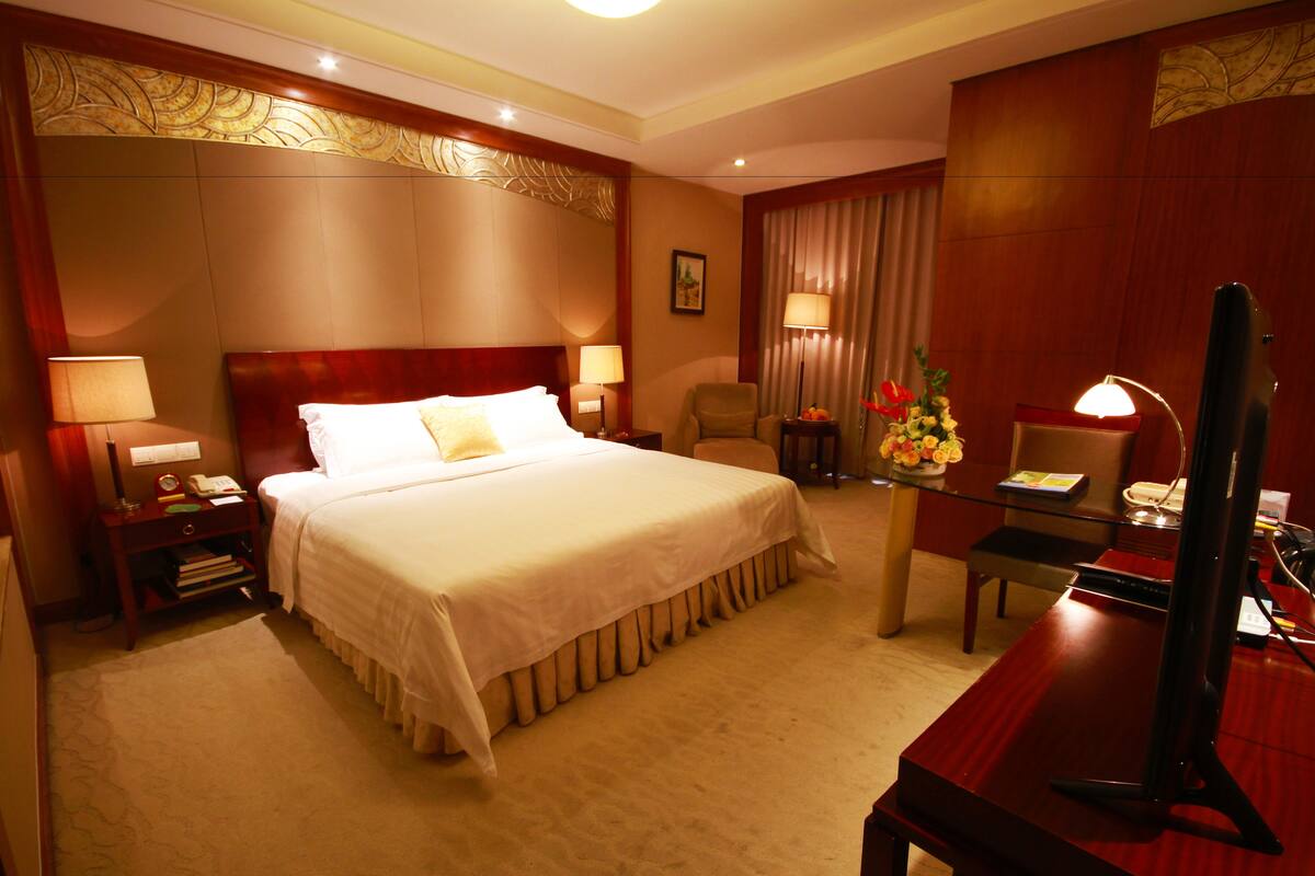 A hotel room with a large bed, two bedside tables with lamps, a desk with a computer, and a chair.