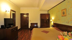 A hotel room with a bed, a television on a dresser, a wooden wardrobe, a nightstand, and a wall-mounted lamp. - Qutub Residency (New Delhi)