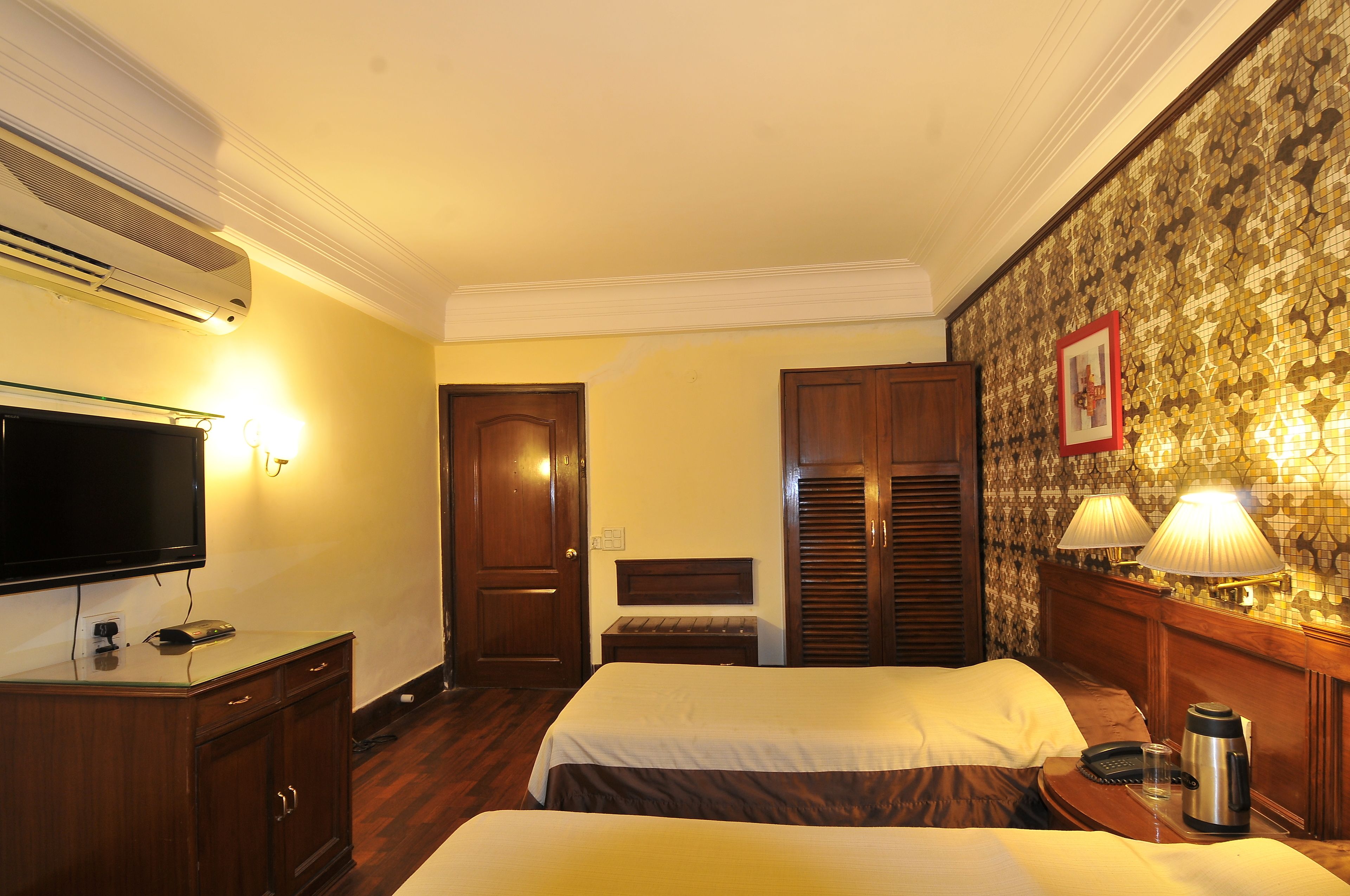 Habitación de hotel con dos camas, un televisor, un escritorio con lámpara y aire acondicionado instalado en la pared.