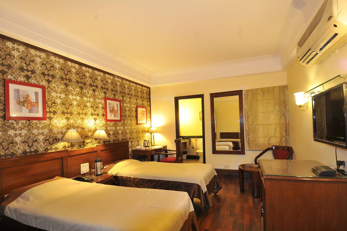 A hotel room with two beds, a desk, a chair, a TV, and a mirror.