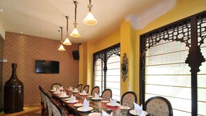 A dining area with a long table set for multiple guests, chairs, a television, and decorative elements like a large bottle and patterned wallpaper. - Qutub Residency (New Delhi)