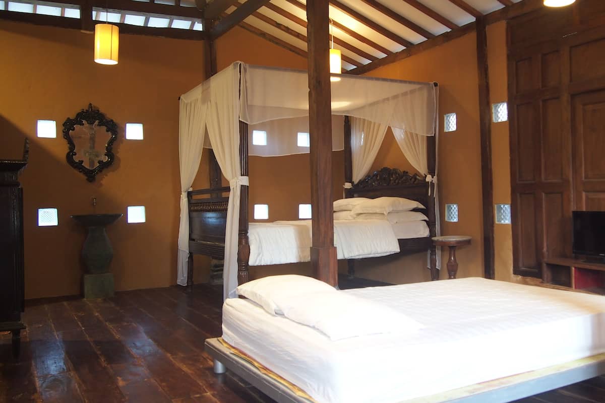 A four-poster canopy bed with white linens, a wooden headboard, and a television on a wooden stand to the right.