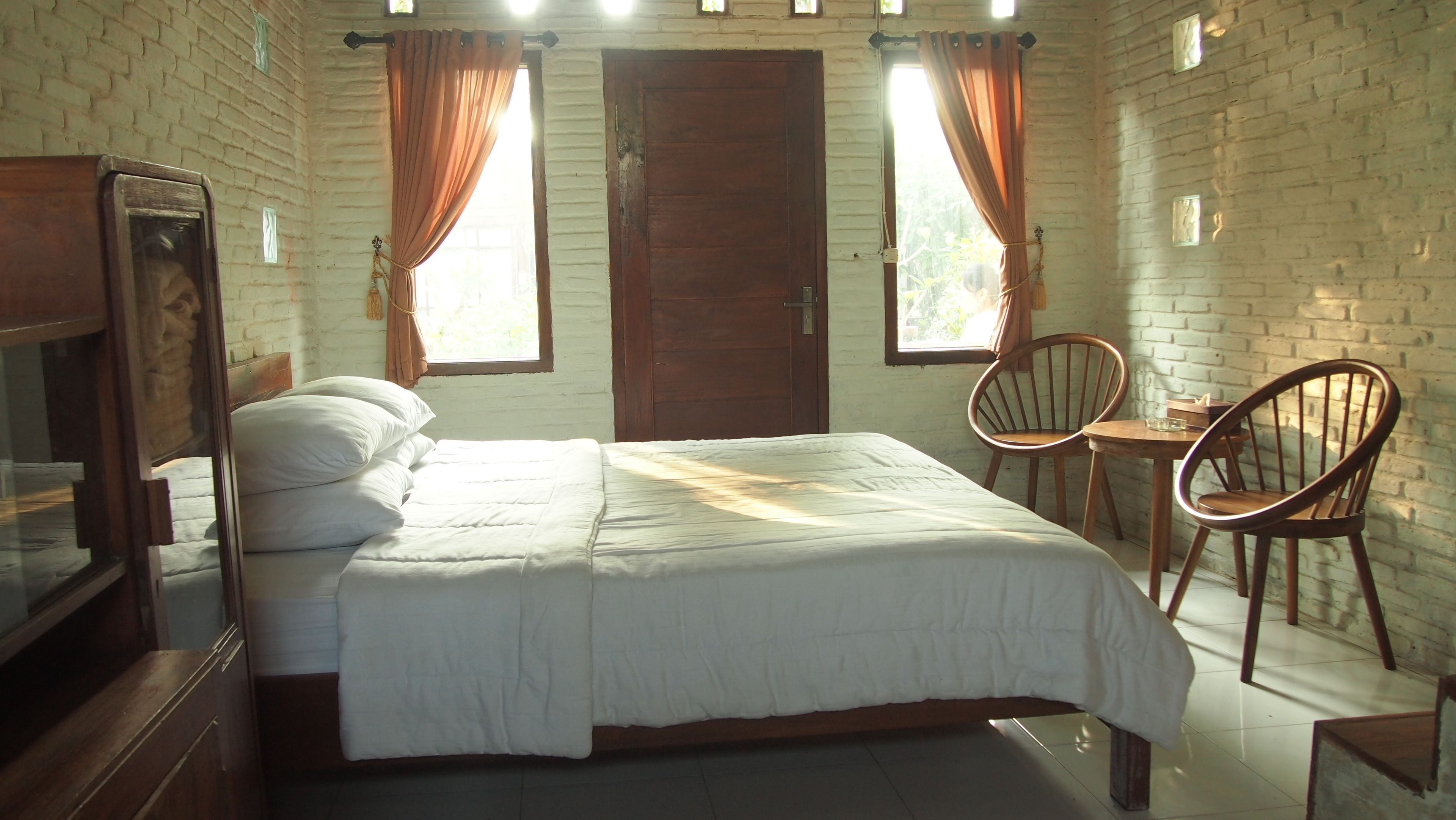Una habitación con una cama, dos sillas de madera, una mesita y un televisor.