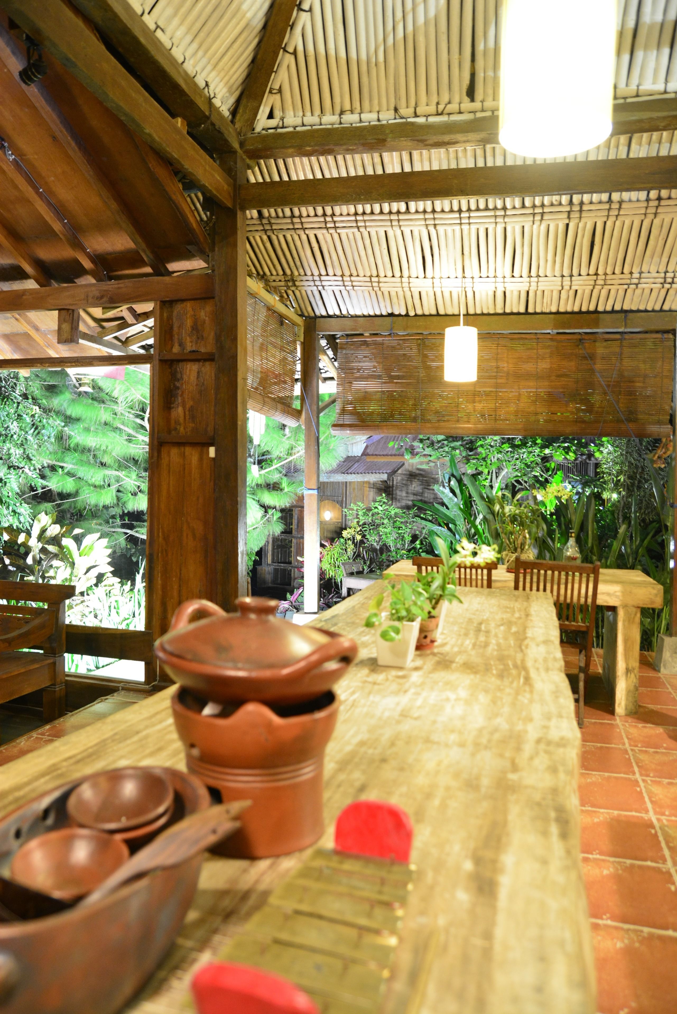 A rustic dining area with a long wooden table, terracotta pots, and wooden chairs.