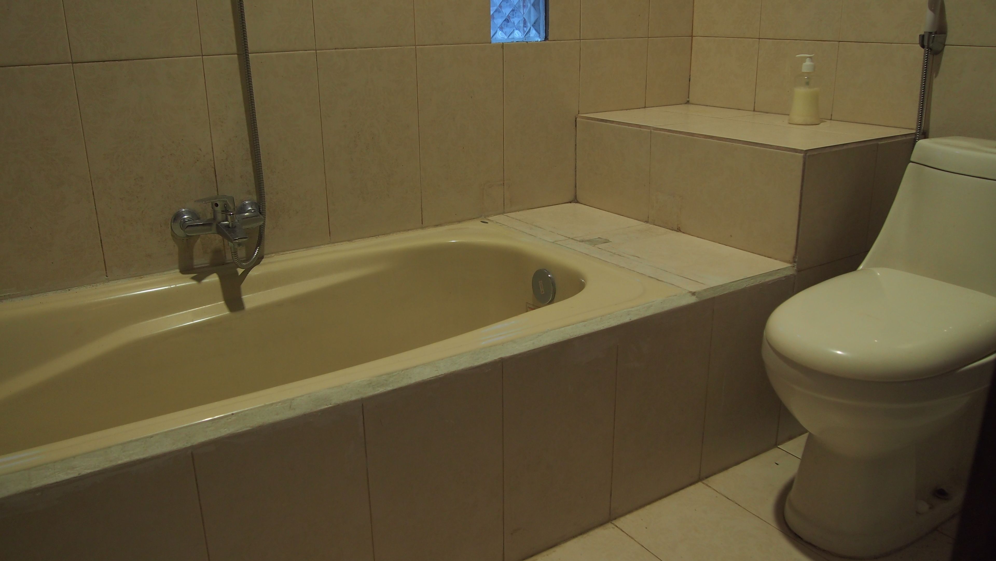 A bathroom with a bathtub, a toilet, and a small shelf with a bottle.