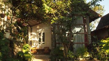 A rustic house with a stone facade, a wooden porch, and a variety of potted plants.