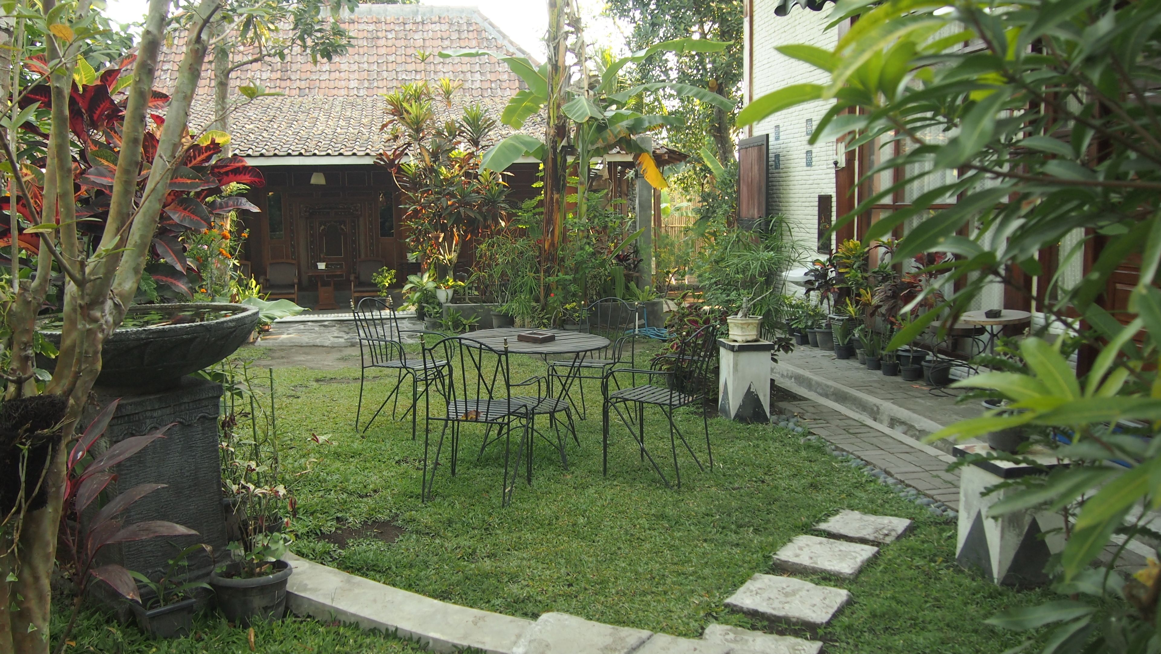 A garden with a table and chairs, surrounded by potted plants and a stone pathway.