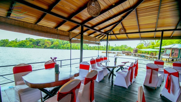 A covered outdoor dining area with tables and chairs, overlooking a body of water and greenery. - Shiny Lakeside Resort (Hikkaduwa)