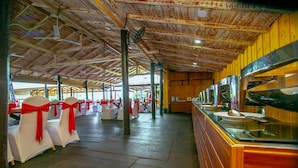 A spacious indoor area with rows of white chairs tied with red sashes, a long counter with a glass top, and a wooden ceiling with visible beams. - Shiny Lakeside Resort (Hikkaduwa)