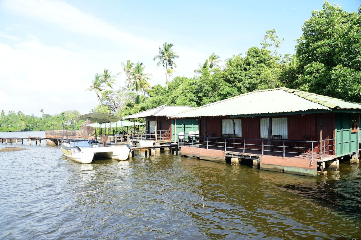 Floating houses with a waterway in between, surrounded by greenery and palm trees.