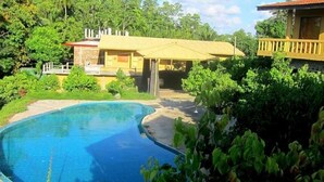 A swimming pool surrounded by lush greenery and a yellow building with a balcony. - Shiny Lakeside Resort (Hikkaduwa)