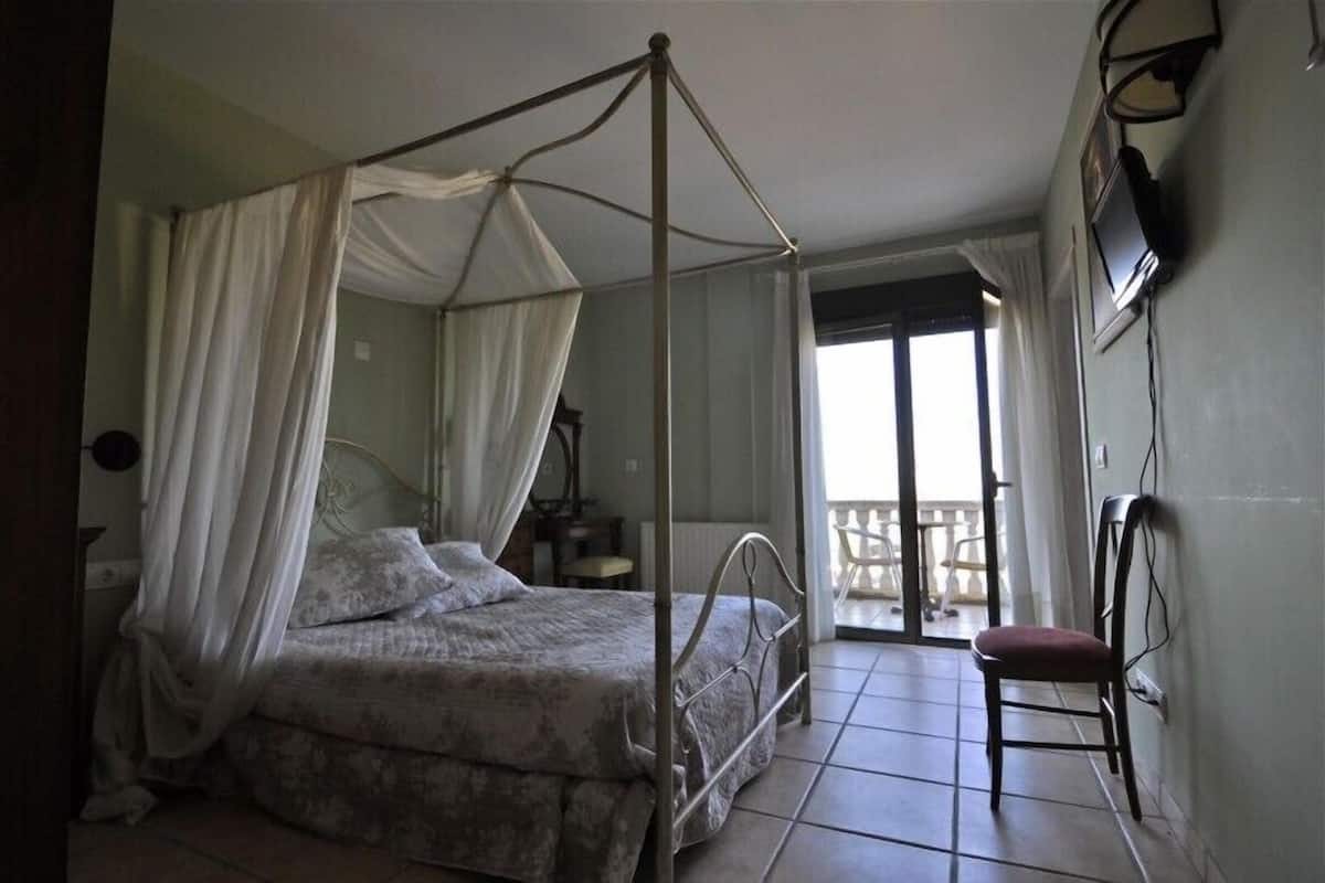 A four-poster bed with a canopy, a chair, a television mounted on the wall, and a balcony with a chair.