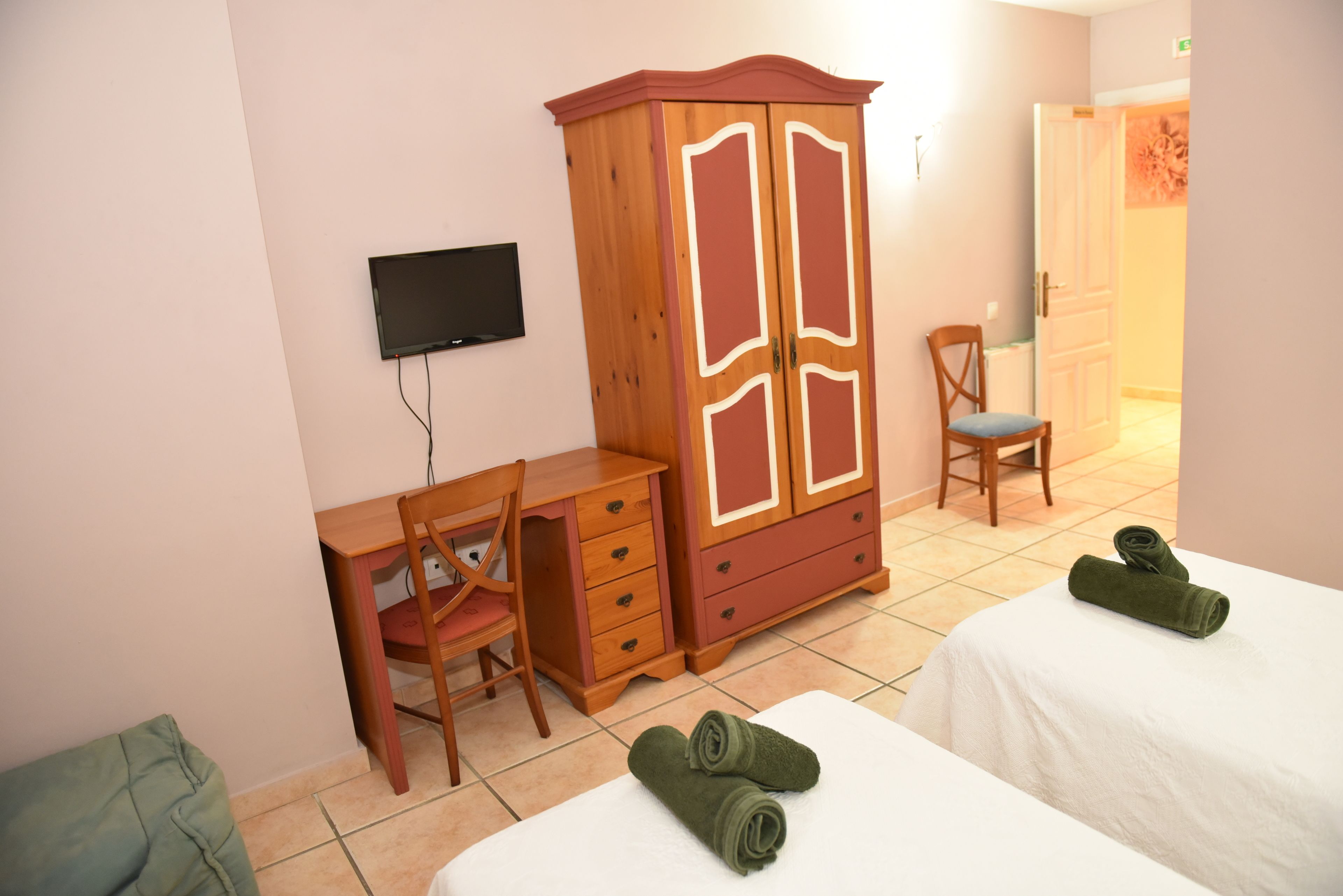 Habitación de hotel con dos camas, un armario de madera, un escritorio con una silla y un televisor en la pared.