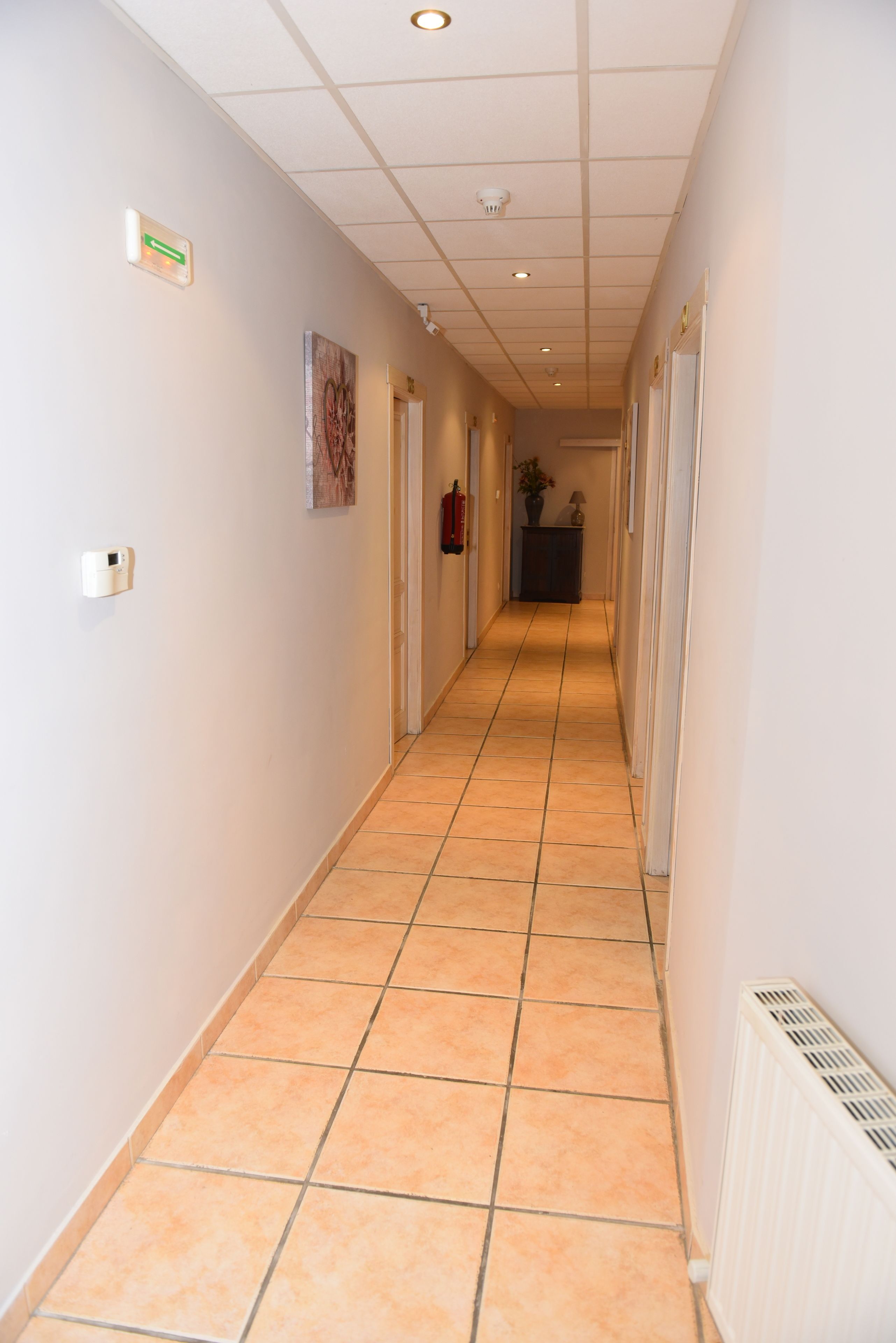 Un long couloir étroit, doté d’un sol carrelé, de murs blancs et d’un plafond pourvu d’un éclairage encastré.