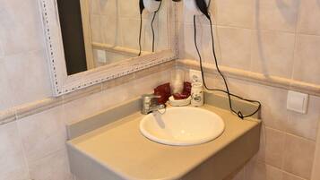 A bathroom with a sink, mirror, hairdryer, and towel rack.