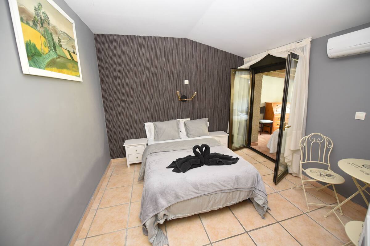 A bedroom with a bed, a nightstand, a chair, a table, and a painting on the wall.