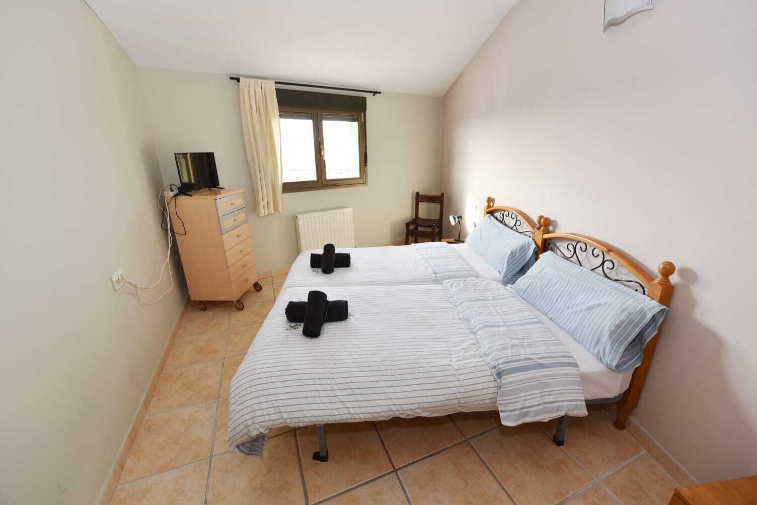 A bedroom with two beds, a dresser, a chair, a window, and a radiator.