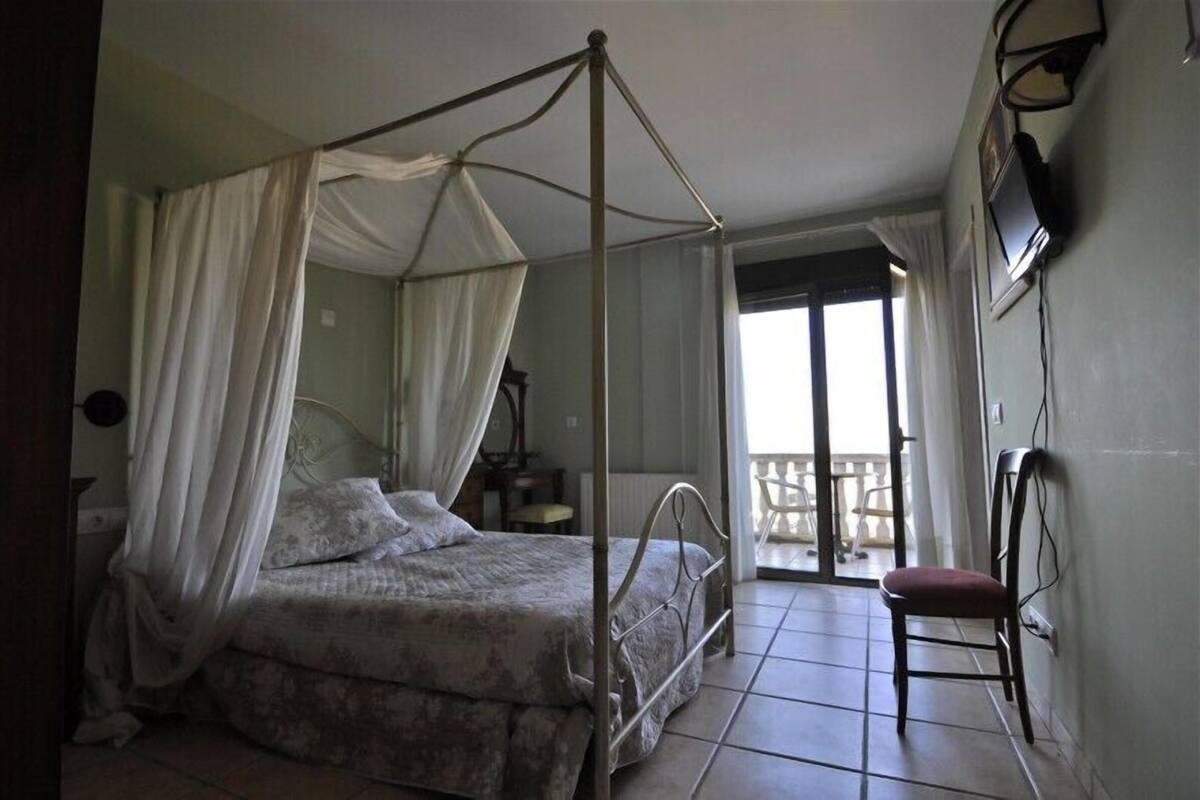 A four-poster bed with a canopy, a chair, a television mounted on the wall, and a balcony with a chair.