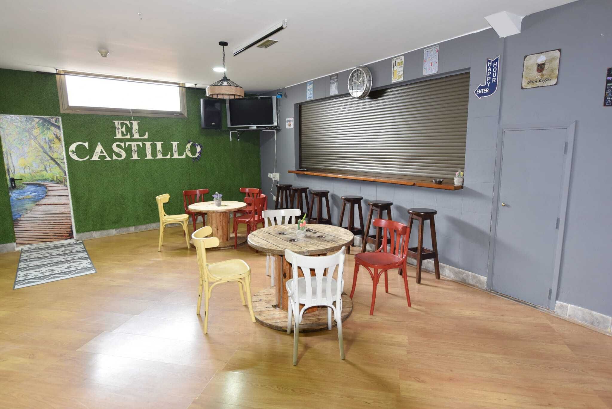 Un comedor con una mesa redonda de madera y sillas, un televisor montado en la pared, y un letrero que dice "EL CASTILLO".