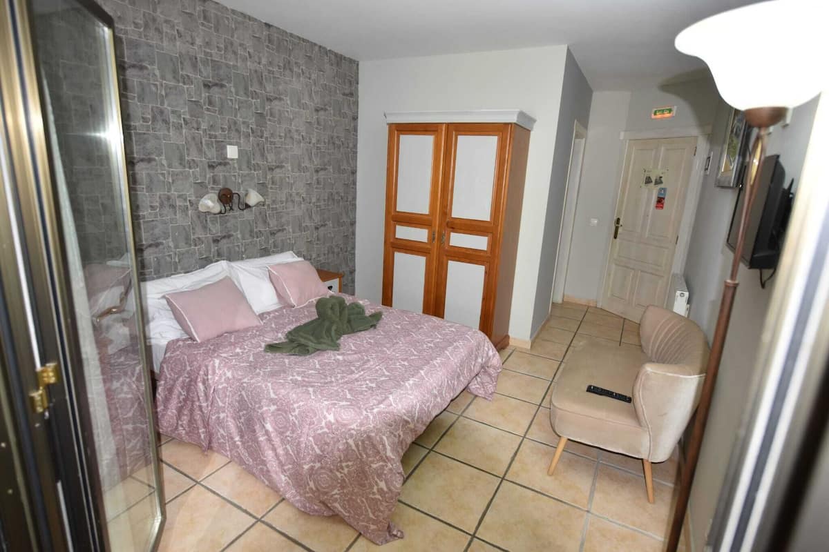 A bedroom with a bed, a chair, a wardrobe, and a stone wall.