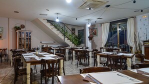A restaurant with multiple wooden tables and chairs, a staircase, and a view of the outside through large windows. - El Castillo (Larraga)