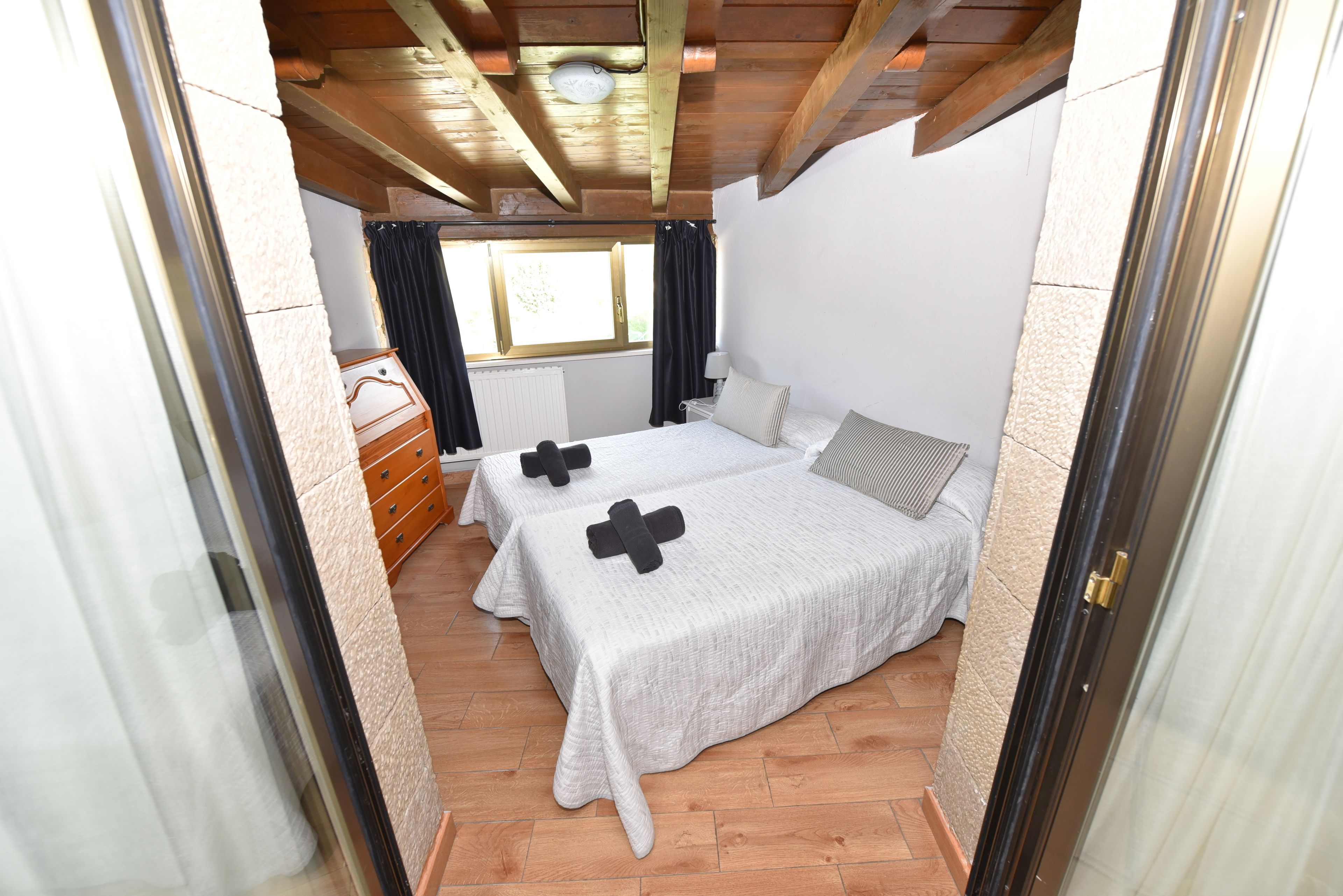 Un dormitorio con dos camas, suelo de madera, una ventana con cortinas y techo de madera.