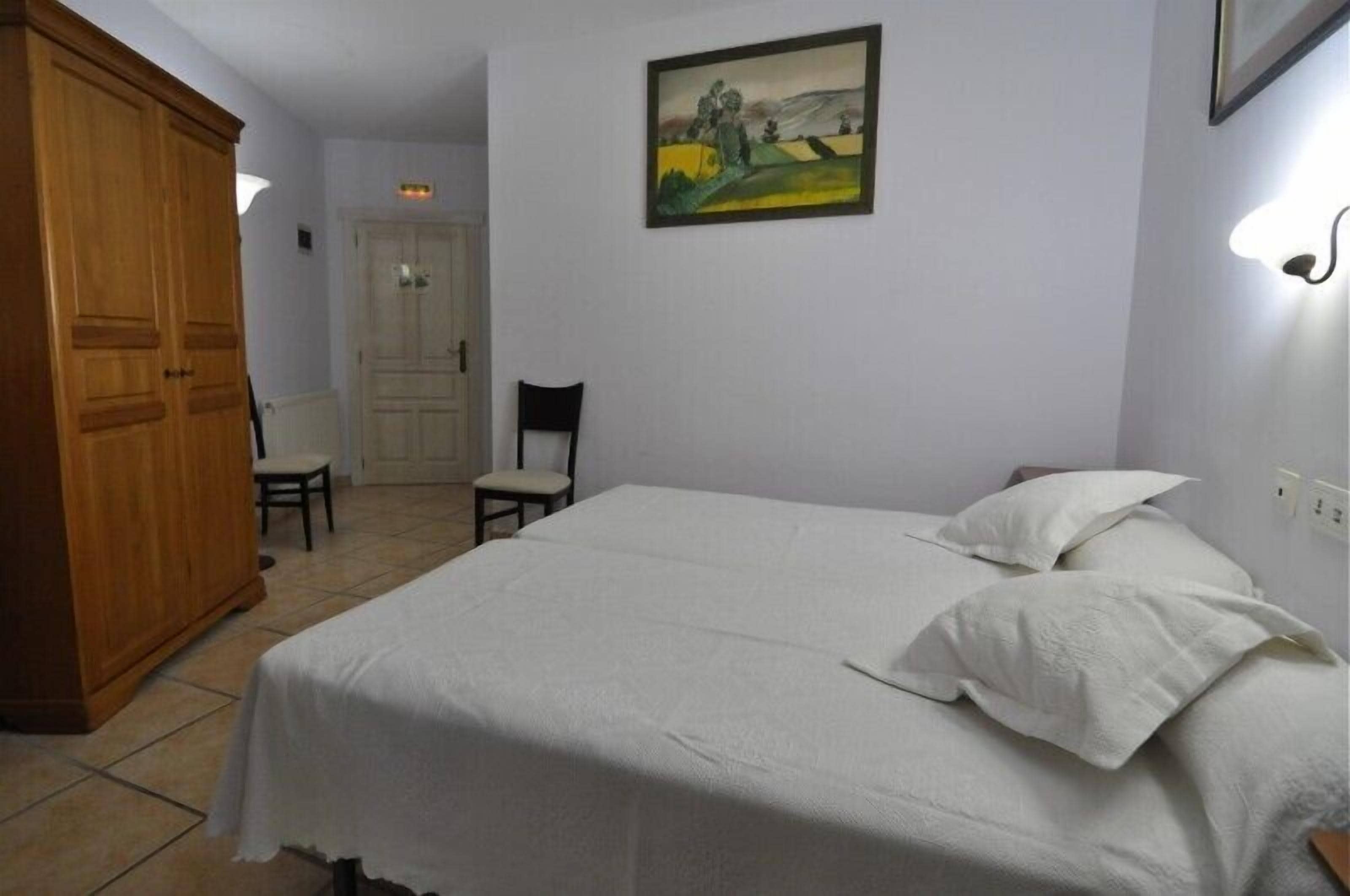 A bedroom with a bed, a chair, a wardrobe, and a painting on the wall.