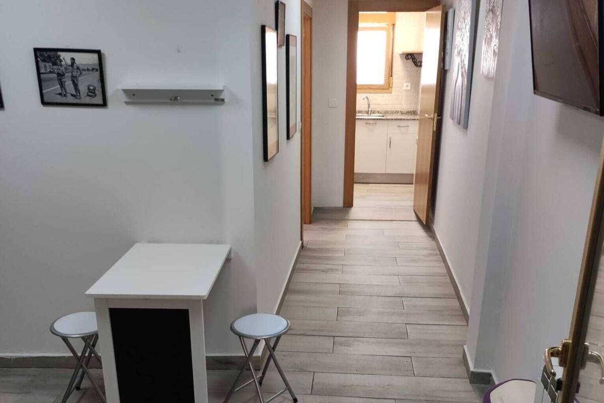 A hallway with a table and chairs, a toilet, and framed pictures on the walls.