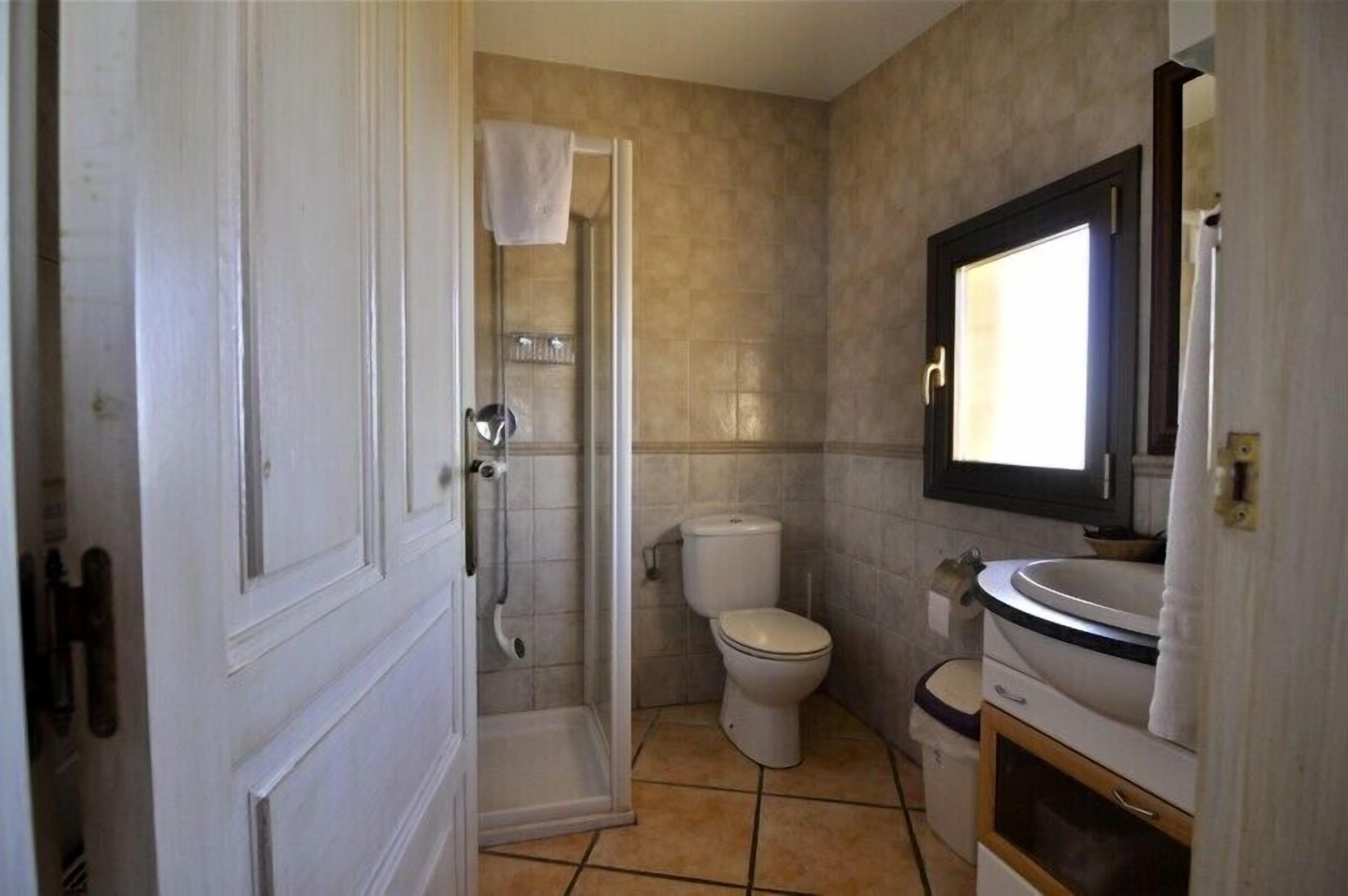 Een badkamer met douche, toilet, wastafel en spiegel.