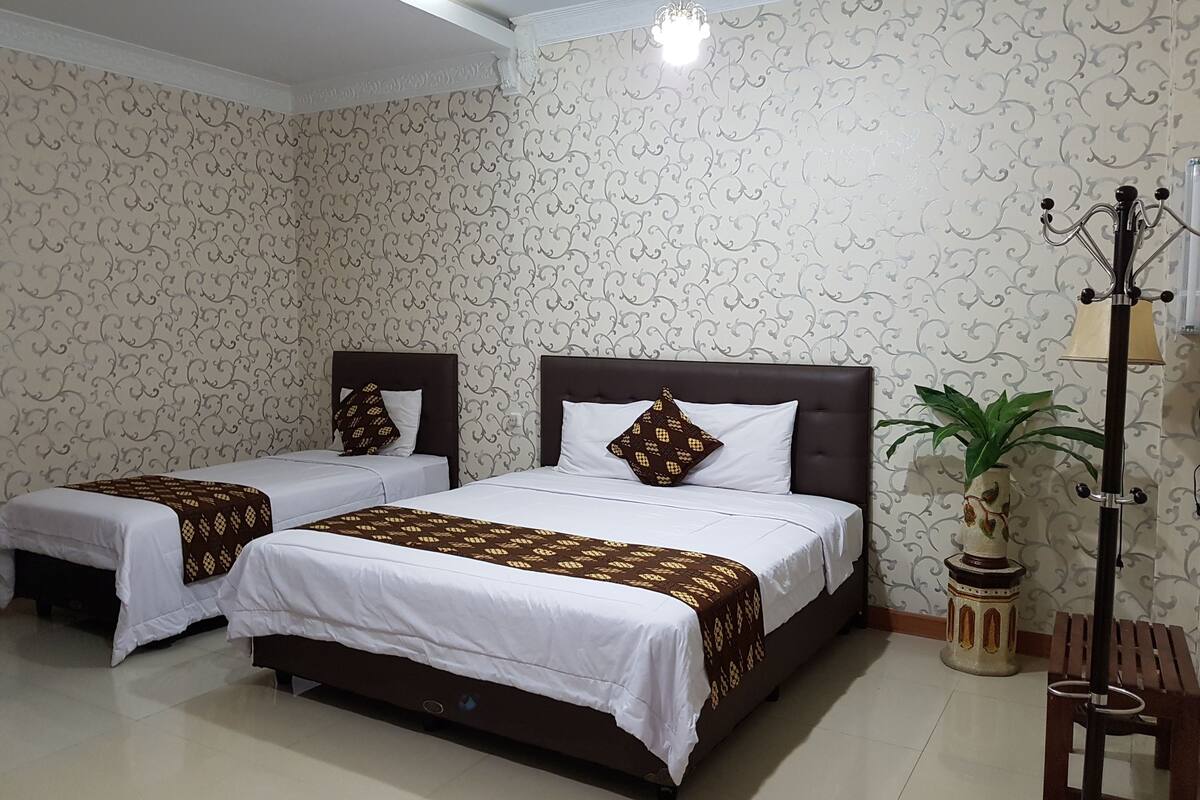 A hotel room with two beds, patterned wallpaper, a potted plant, and a floor lamp.