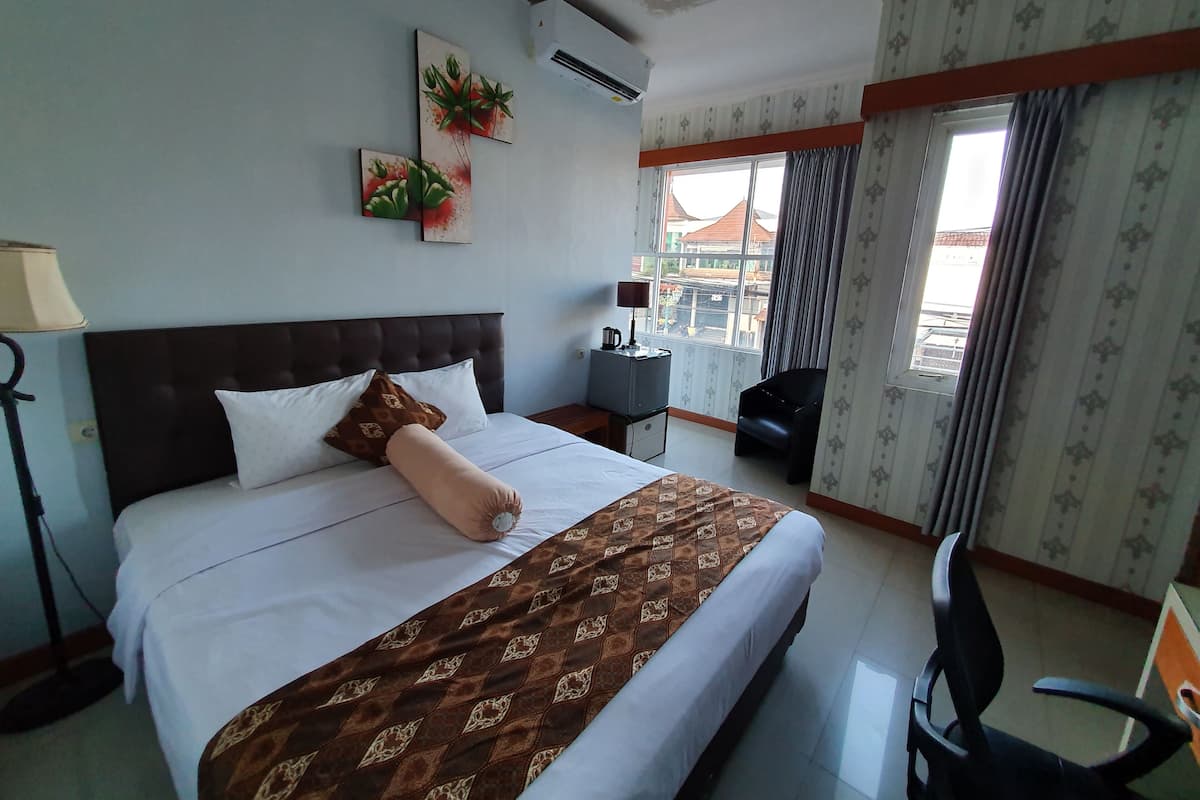 A hotel room with a large bed, a desk, a chair, and a view of the city through the window.