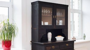 Un mueble de madera oscura con puertas de cristal, un jarrón blanco y una planta en maceta roja sobre un alféizar blanco.