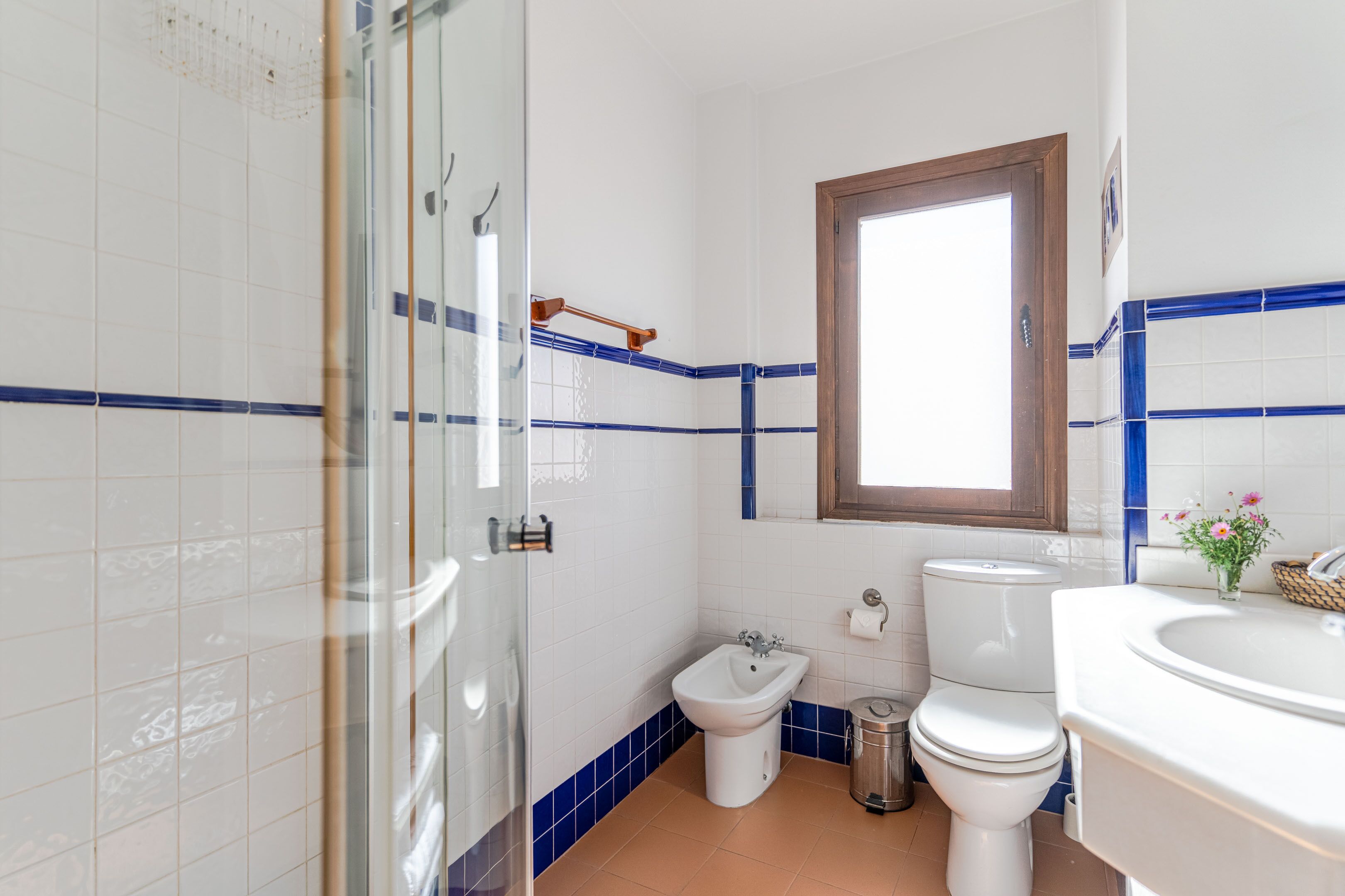 Een badkamer met een douchecabine van glas, een bidet, toilet en een wastafel met spiegel erboven.