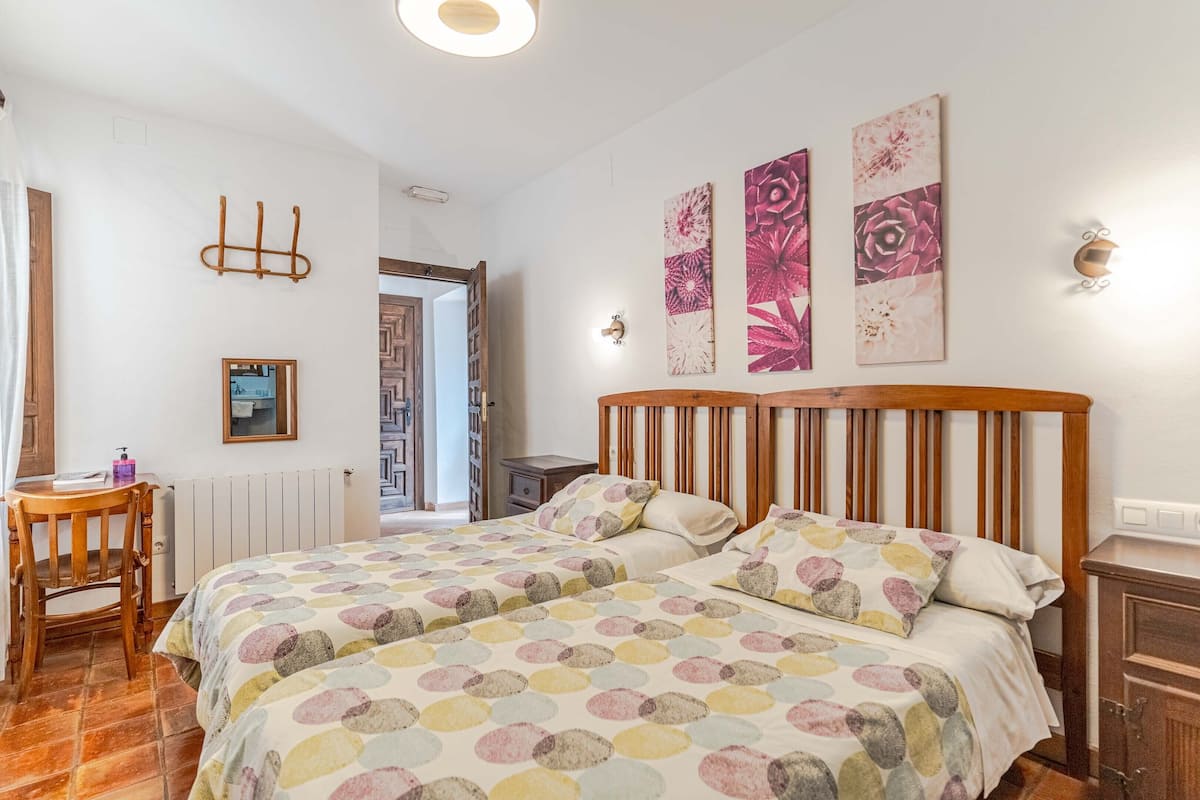 Un dormitorio con dos camas, cabeceros de madera, una mesita con una silla y un radiador.