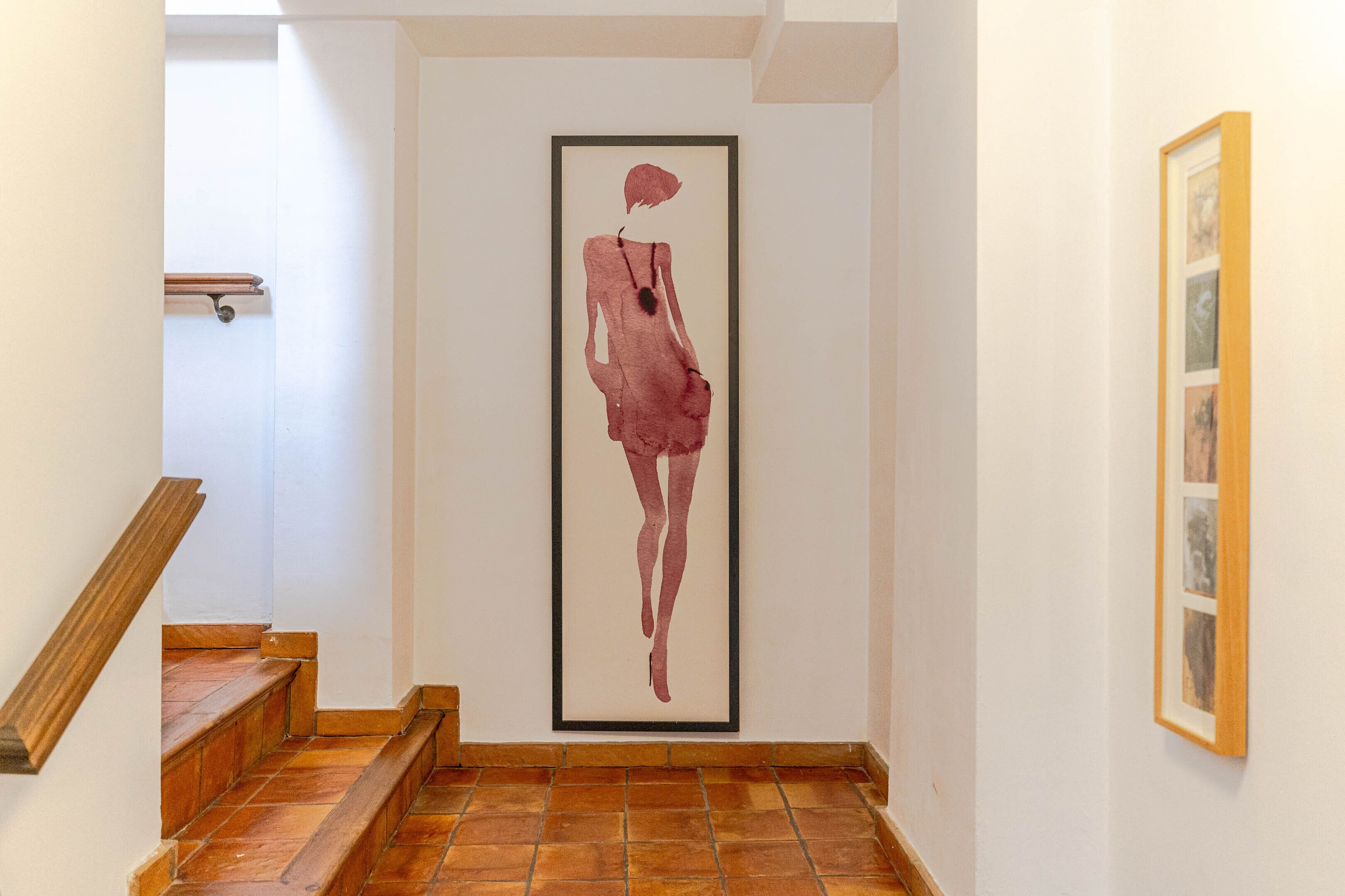 Een hal met een gekaderd kunstwerk van een figuur aan de muur, houten trap en betegelde vloer.