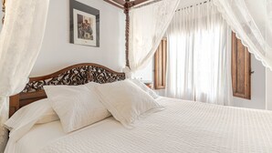 Een hemelbed met witte lakens en een houten hoofdbord.